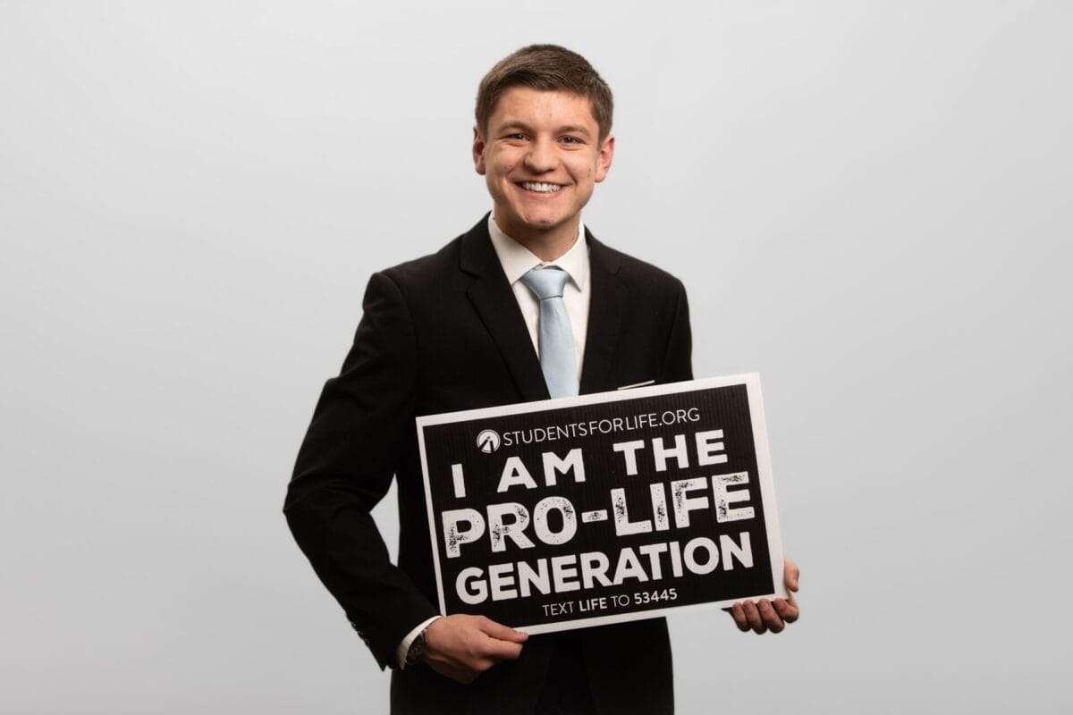 A man in a suit holds a sign that reads, "I AM THE PRO-LIFE GENERATION."
