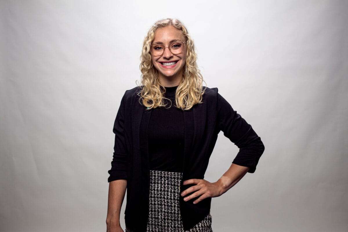 A woman with her hand on her hip smiles at the camera.