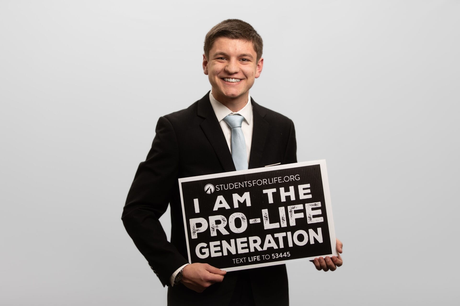 A man in a suit holds a sign that reads, "I AM THE PRO-LIFE GENERATION."