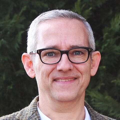 A man wearing glasses smiles at the camera.