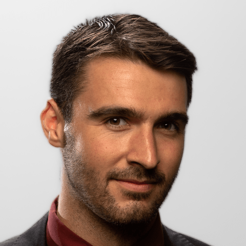 A man smiles while looking slightly sideways towards the camera.