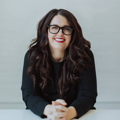 A woman with glasses and long, dark hair smiles at the camera.