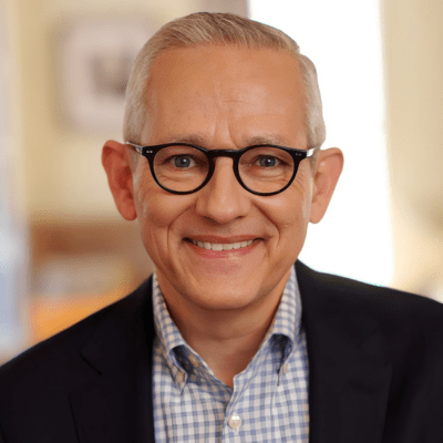 A man in a suit and glasses smiles at the camera.
