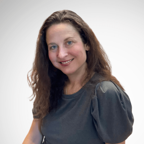 A woman with brown hair tilts her head and smiles at the camera.