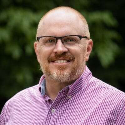 A man with a goatee and glasses smiles at the camera.