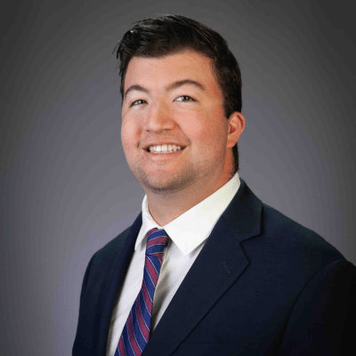 A man in a suit is turned slightly and smiles at the camera.
