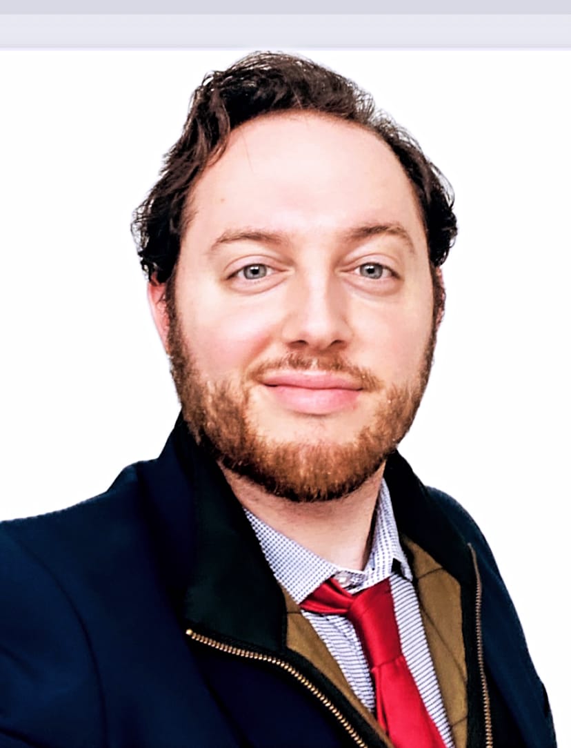 A man in a suit is turned sideways and smiles at the camera.