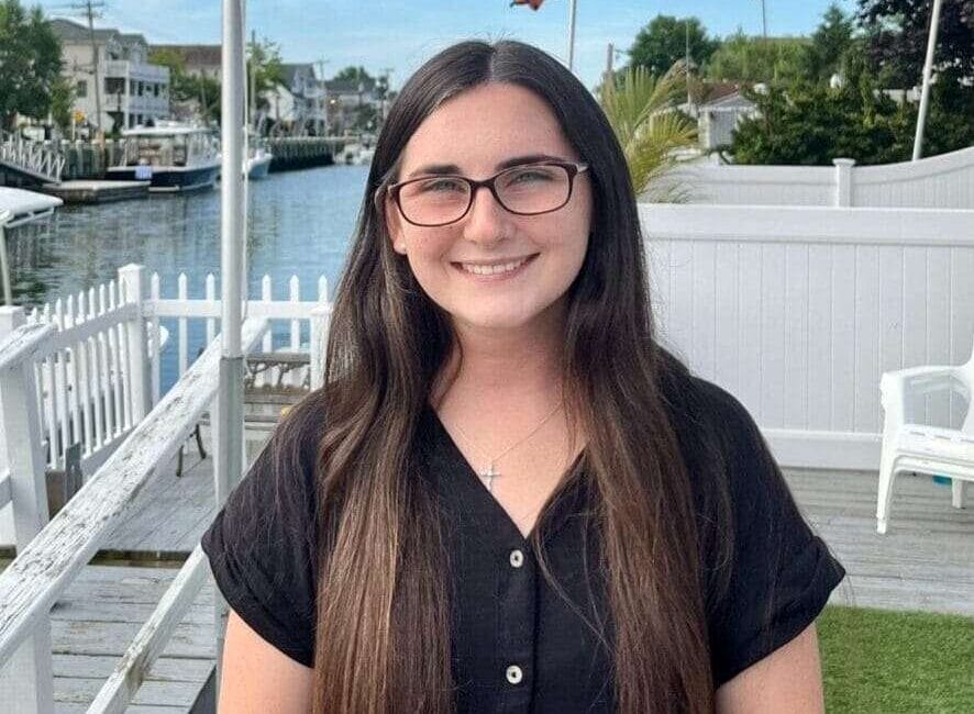 A woman with long hair and glasses smiles at the camera.