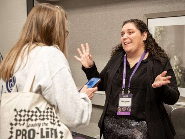 A woman smiles while speaking with another woman.