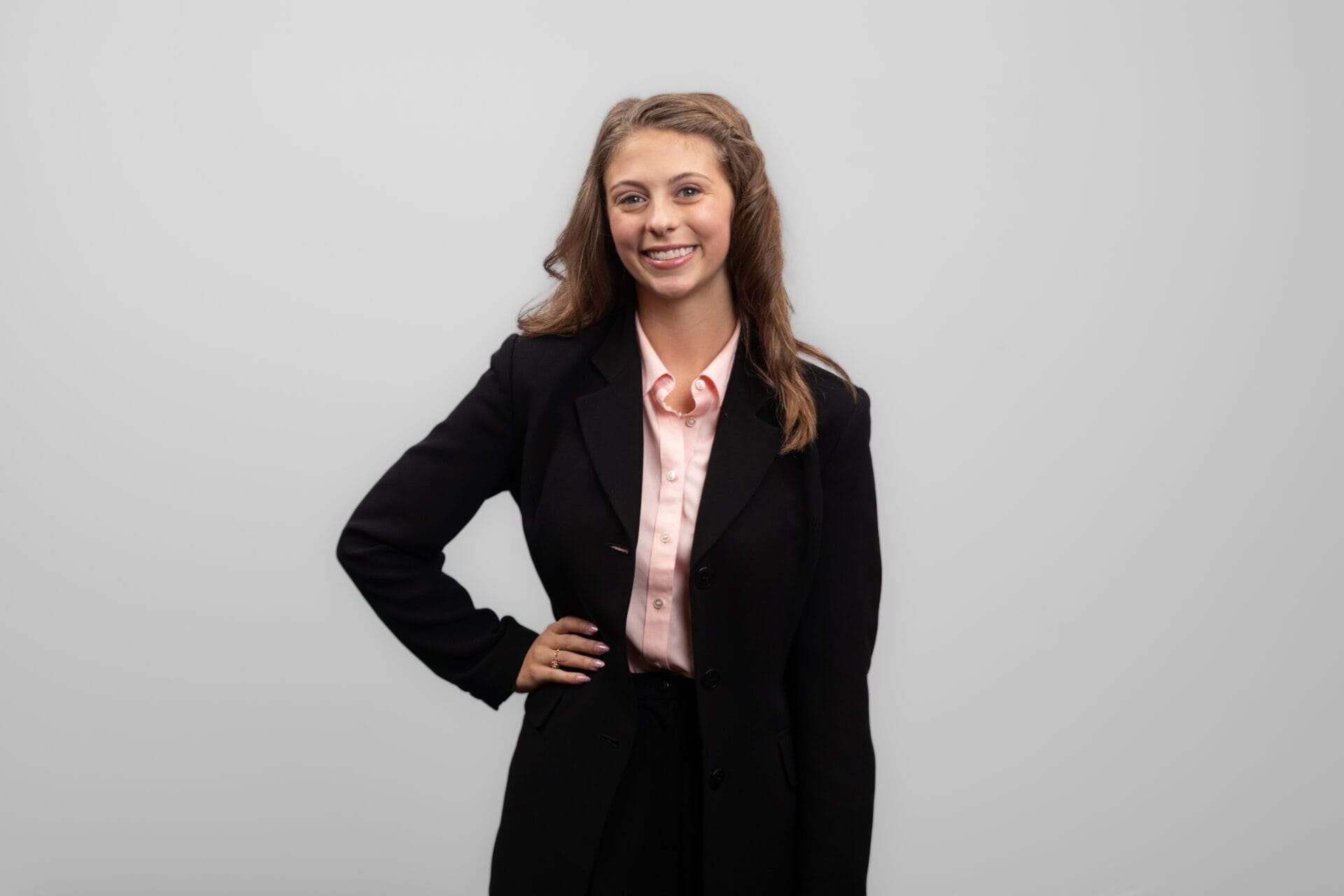 A woman in a black suit smiles while standing with her hand on her hip.