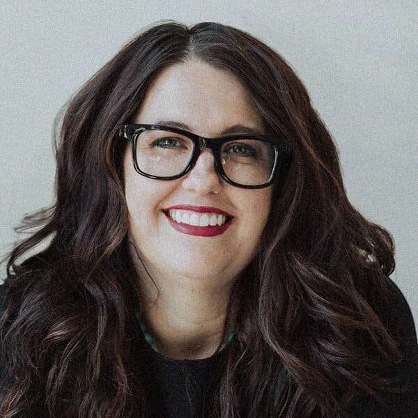 A woman with wavy hair and glasses smiles at the camera.
