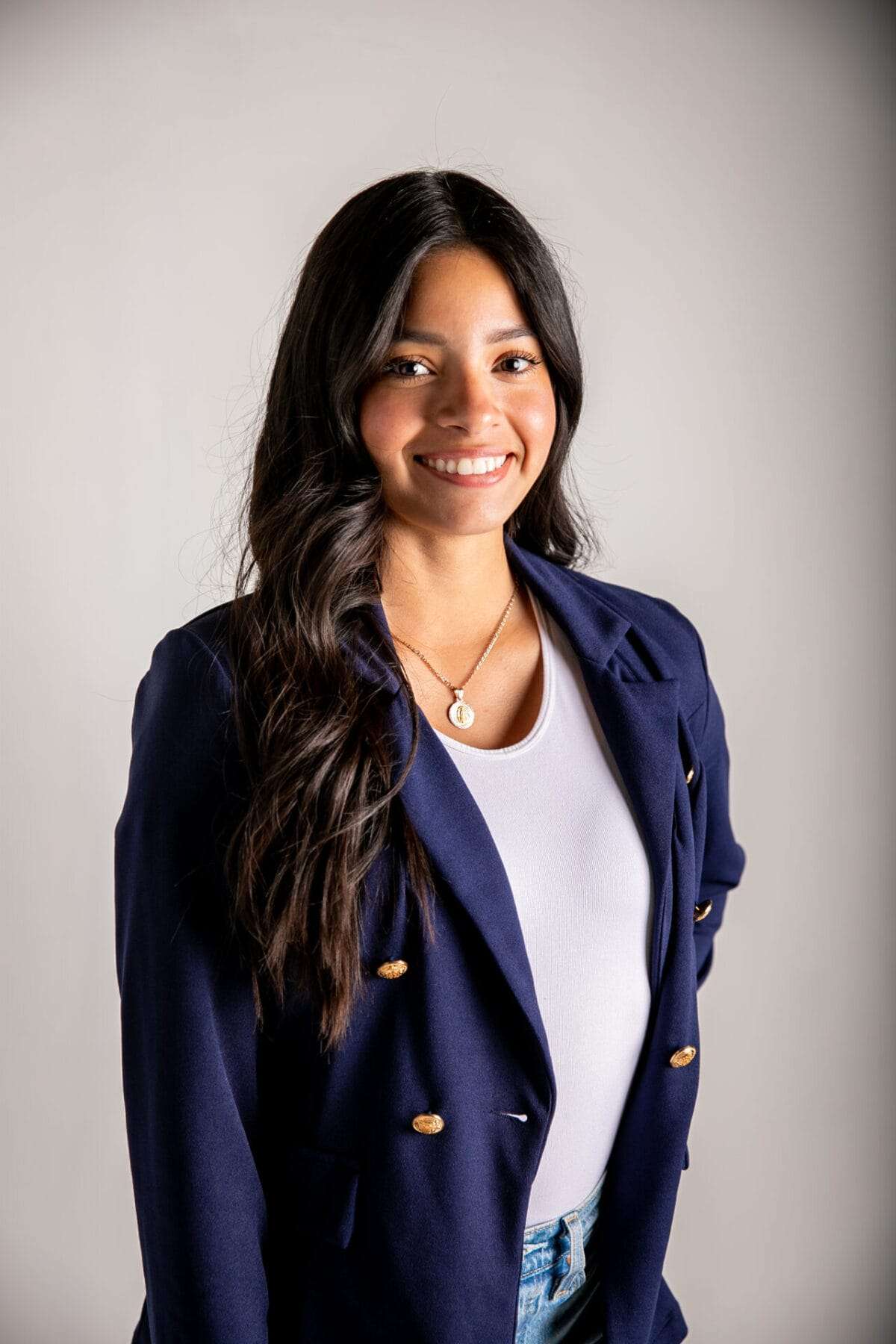 A woman with curly hair wears a suit jacket and smiles at the camera.