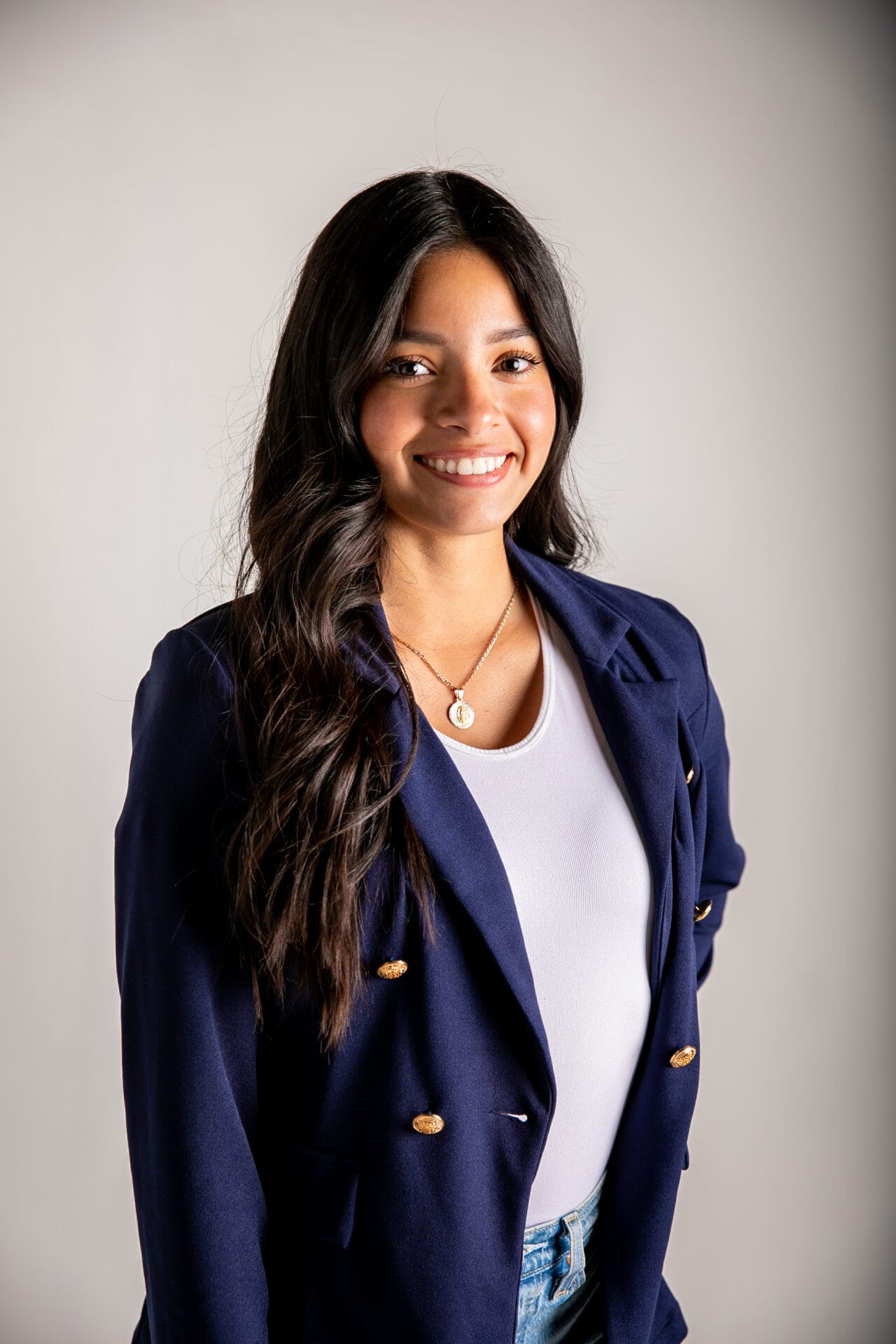 A woman with curly hair wears a suit jacket and smiles at the camera.