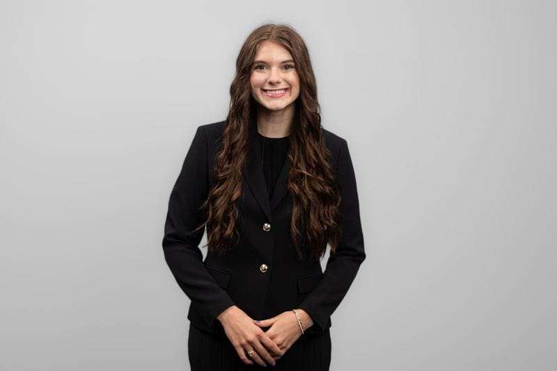 A woman holds her hands together In front of her and smiles at the camera.