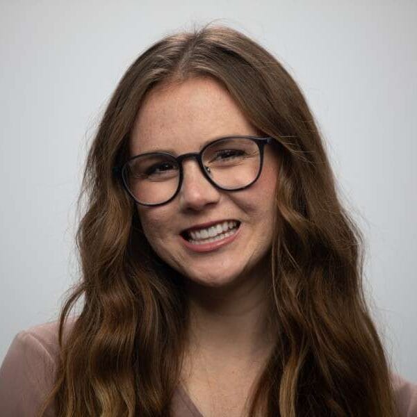 A woman with wavy hair and glasses smiles at the camera.
