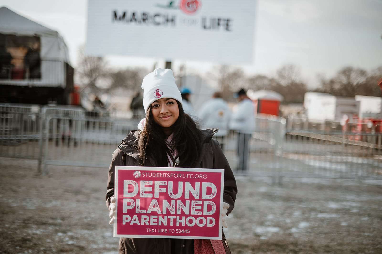 Pro-Life Protester holds up sign reading: studentsforlife.org, Defund Planned Parenthood, Text Life to 53445