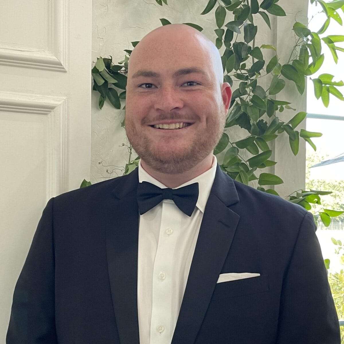 A man in a tuxedo and bowtie smiles at the camera.