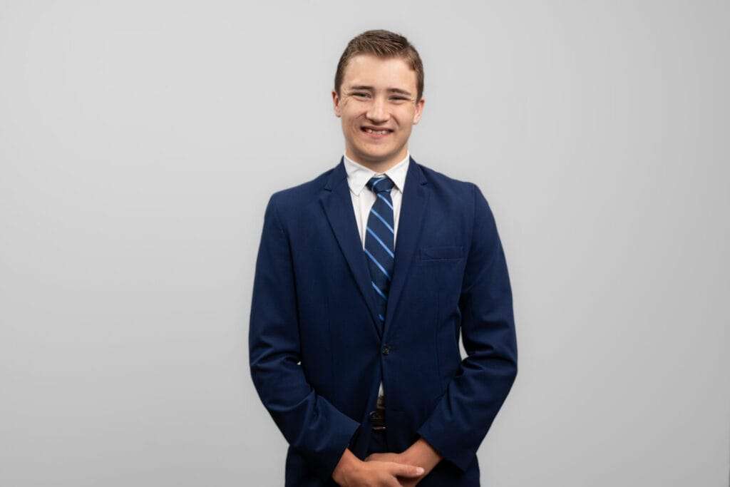 A man in a suit holds his hands in front of him and smiles at the camera.