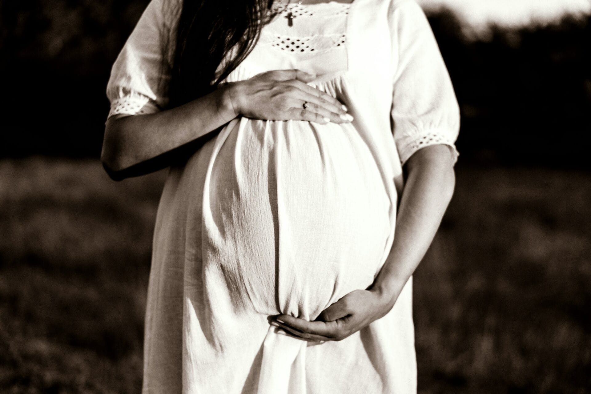 A pregnant woman holds one hand on top of her stomach and the other beneath it.
